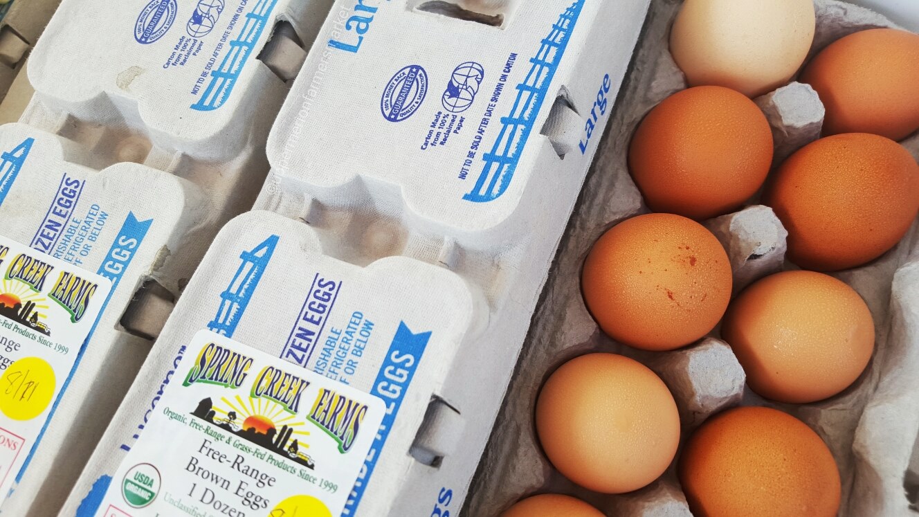 eggs1 Carton of free-range brown eggs from Spring Creek Farms, featuring a dozen eggs with various shades of brown, alongside a second carton labeled as "frozen eggs." The packaging highlights organic and grass-fed farming practices.